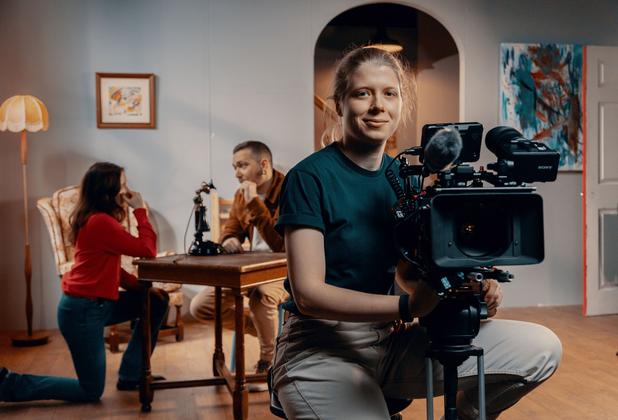 A student using a film camera with two people behind him on set