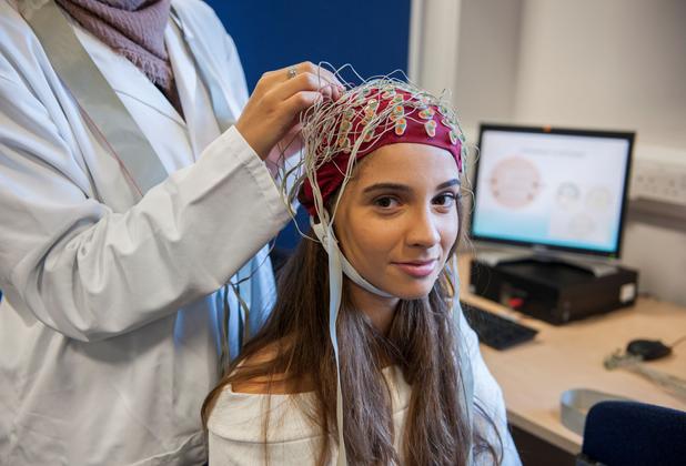 A woman sits with a therapist who is applying electrodes to a cap on her head