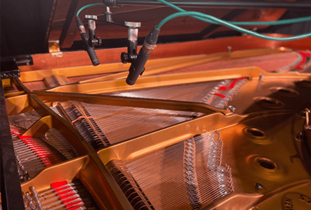 Close-up of microphones recording inside an open grand piano, capturing strings and hammers for a BA (Hons) Music for Film and Games course.