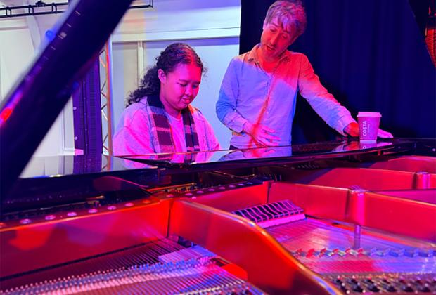 Student at piano with teacher watching on.