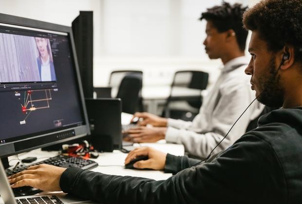 Students edit digital media projects on computers in a graphic design studio.