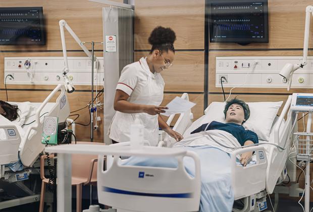 A nurse stands next to a dummy in a hospital bed