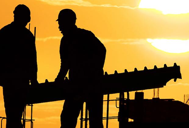Dark silhouettes of two people working on a dockyard at sunset