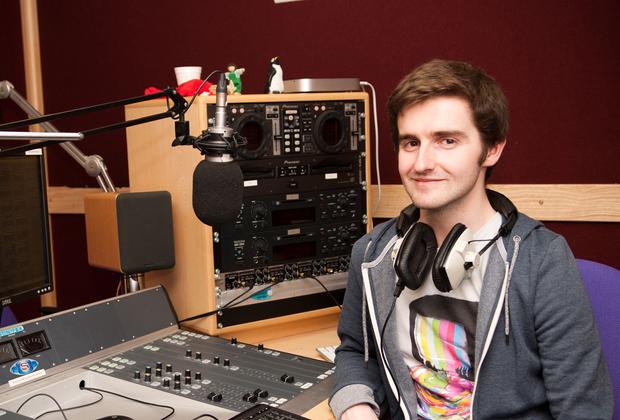 Male student wearing headphones sitting in front of a music mixer device
