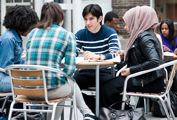 Four students sitting around a table at the Mdx Uni quad, chatting