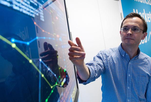 lecturer pointing to financial dashboard on large screen