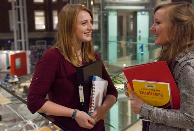 two women holding accounting textbooks have a friendly conversation