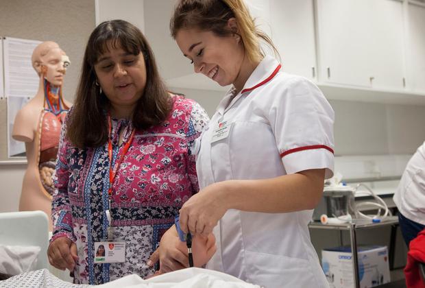 Two nurses assisting a baby in a hospital room.