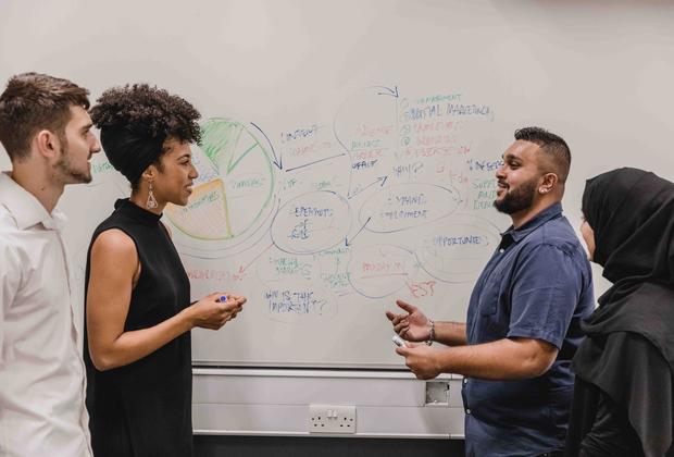 Business management students adding ideas onto a whiteboard