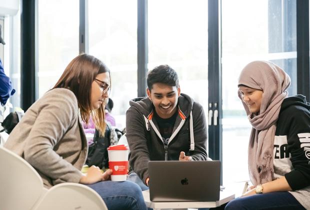 A group of three students gathered round a laptop in a cafe area