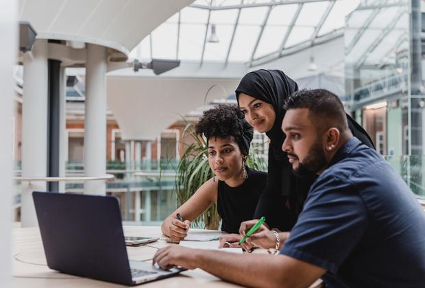 A group of three students looking at a laptop in a building