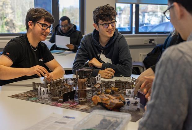 A group of male students sat around games pieces on a table