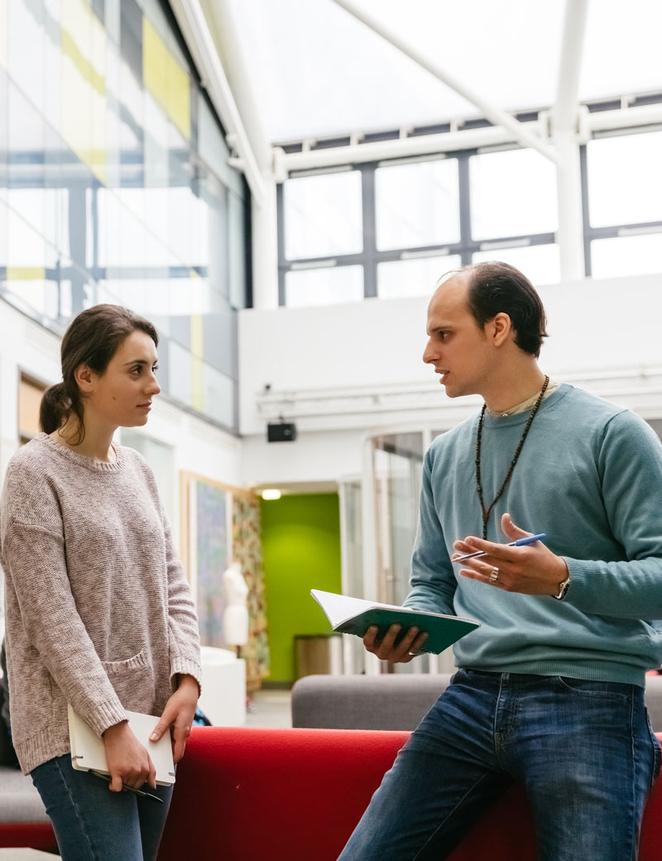 Two adults having a conversation in a well lit campus building