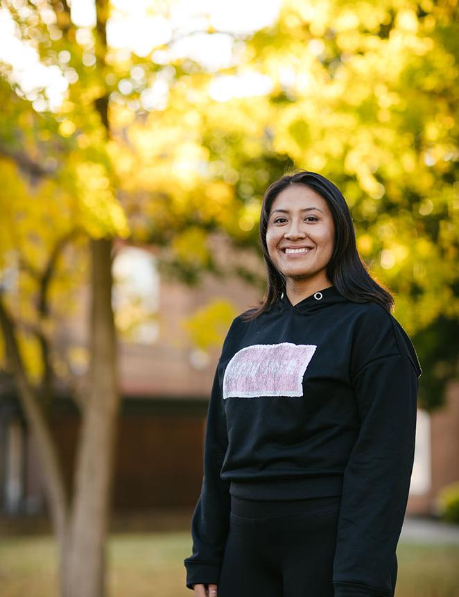 Student smiling in front of autumnal tree