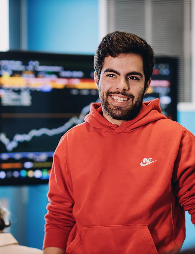 student poses in front of computer showing financial data