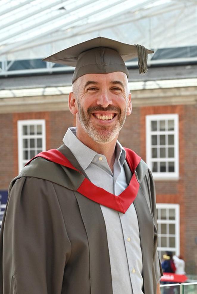 A man in graduation cap and gown poses for a photo in a university building