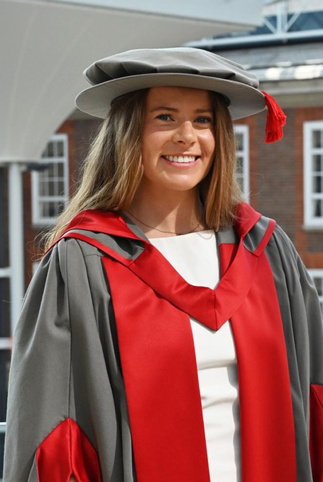 A woman in graduation cap and gown poses for a photo in a university building