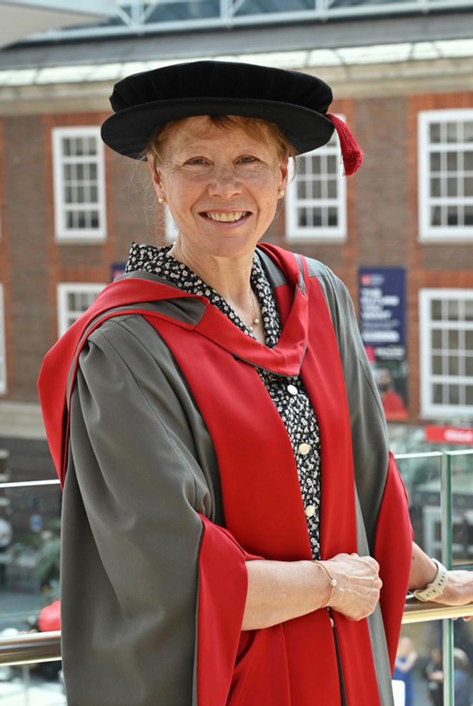 A woman in graduation cap and gown poses for a photo in a university building