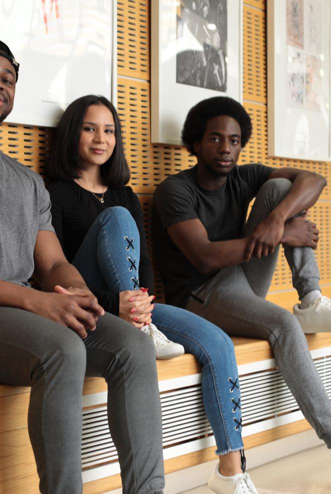 Three young people sitting on a bench in front of a wall, engaged in conversation and enjoying each other's company.