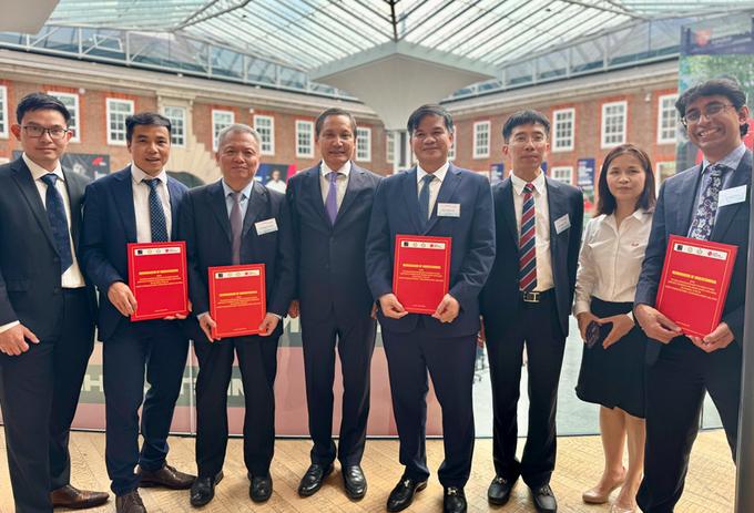 A line-up of visitors to MDX from University of Oxford and Vietnam, four of them holding red certificates representing an MOU between MDX and their institutions