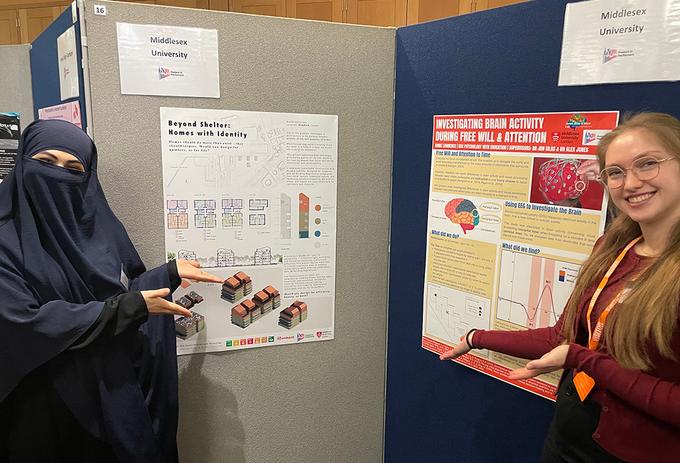 Two students stand either side of a display of posters