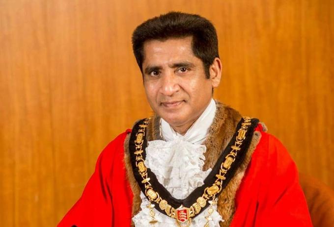 A portrait of a Mayor in his robes of office against a wooden background