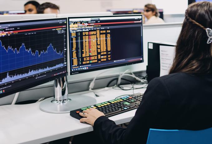A woman suits in front of two computer monitors displaying data in graph and list form