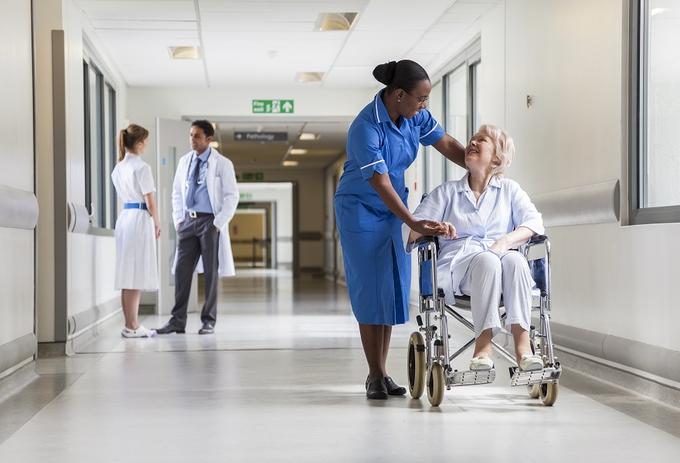 A caring nurse assisting an elderly woman in a wheelchair in a hospital corridor.