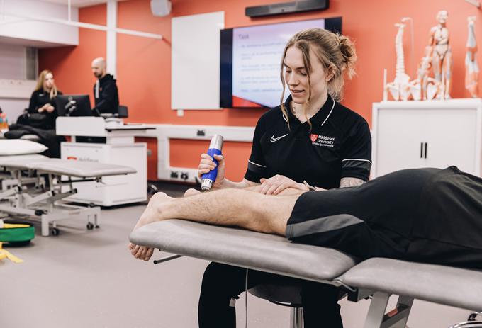 A sports science student massages a person's leg while they are lying on a treatment table