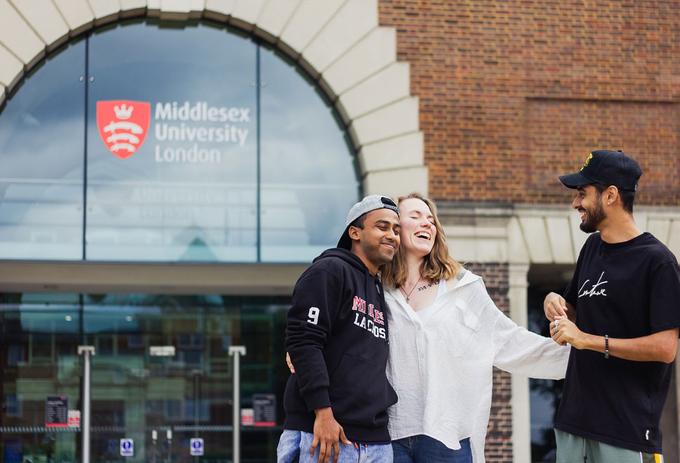 A group of students standing and laughing together outside Middlesex University entrance