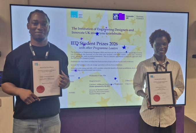 Two award winners holding certificates, with a screen behind them displaying their prize.