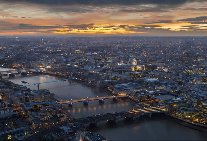 Sunset over London cityscape with recognizable landmarks such as the Thames River, Tower Bridge, and the Shard building.
