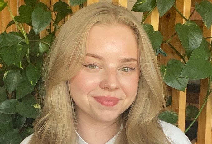 Wilma Claesson smiling while standing in front of a leafy plant