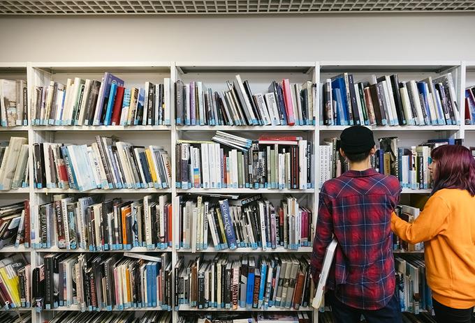 Two students look at books in a library