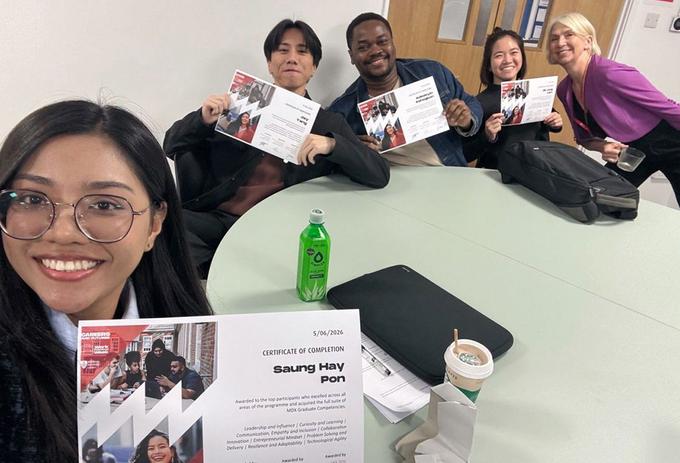Students hold up certificates at a desk