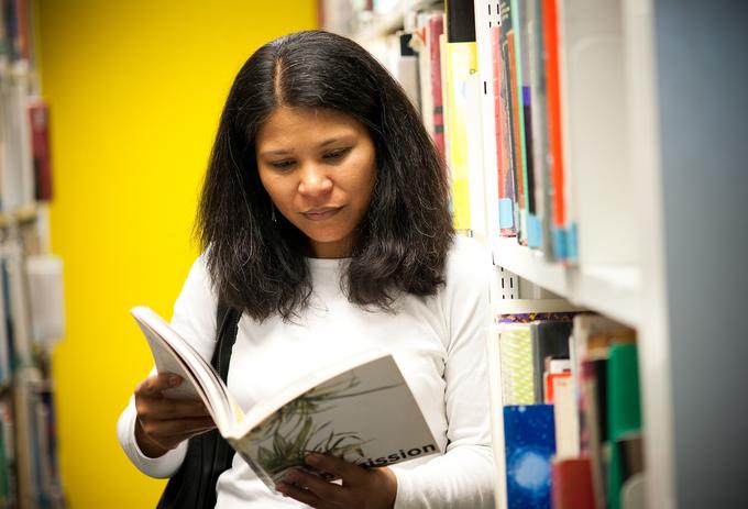 Female student stood in library with textbook open
