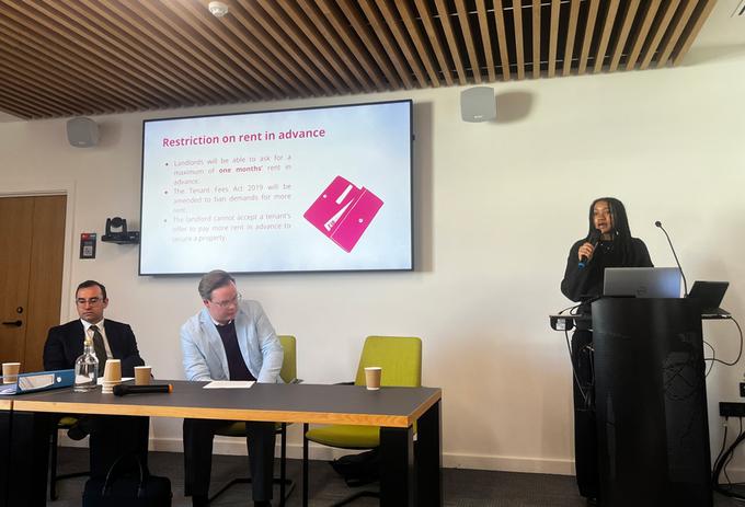 A group of three people at a lecture, one of which is presenting at a podium about the Renters' Rights Act