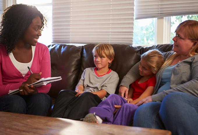 social workers and environmental health practitioner is seating on the sofa with a women and 2 kids