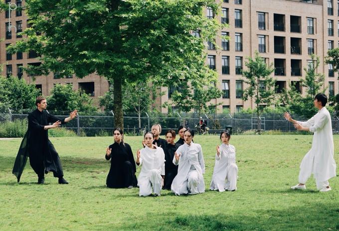 A group of dancers in black and white costumes flowing costumes strike dramatic poses in Colindale Park