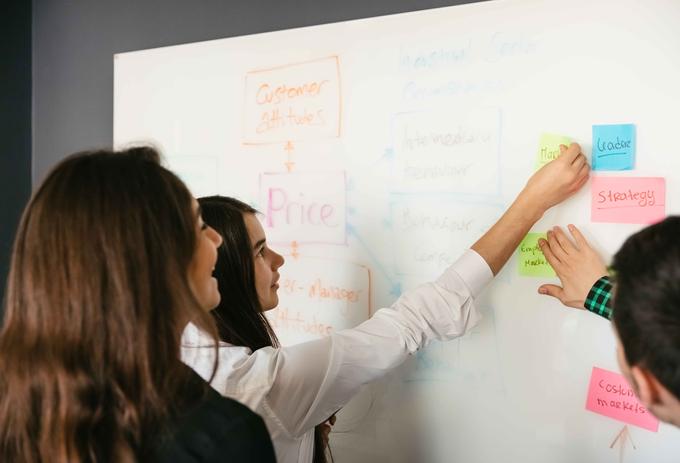Business management students adding ideas onto a whiteboard