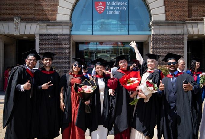 A group of enrobed graduates celebrating in front of the main Middlesex University London entrance