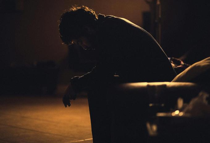 Male sitting in a dark room looking at the floor