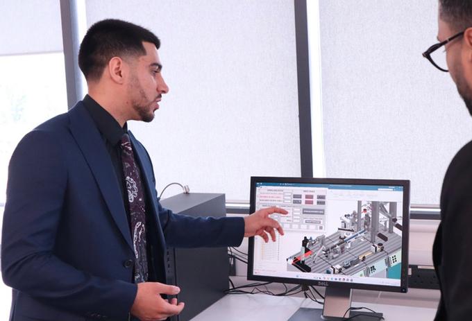 A man in a suit standing in front of mechatronics equipment looking at the camera