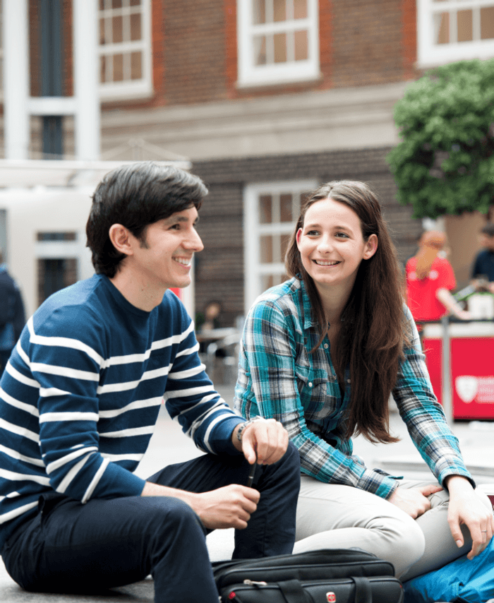male and female students socialising in the quad, college building