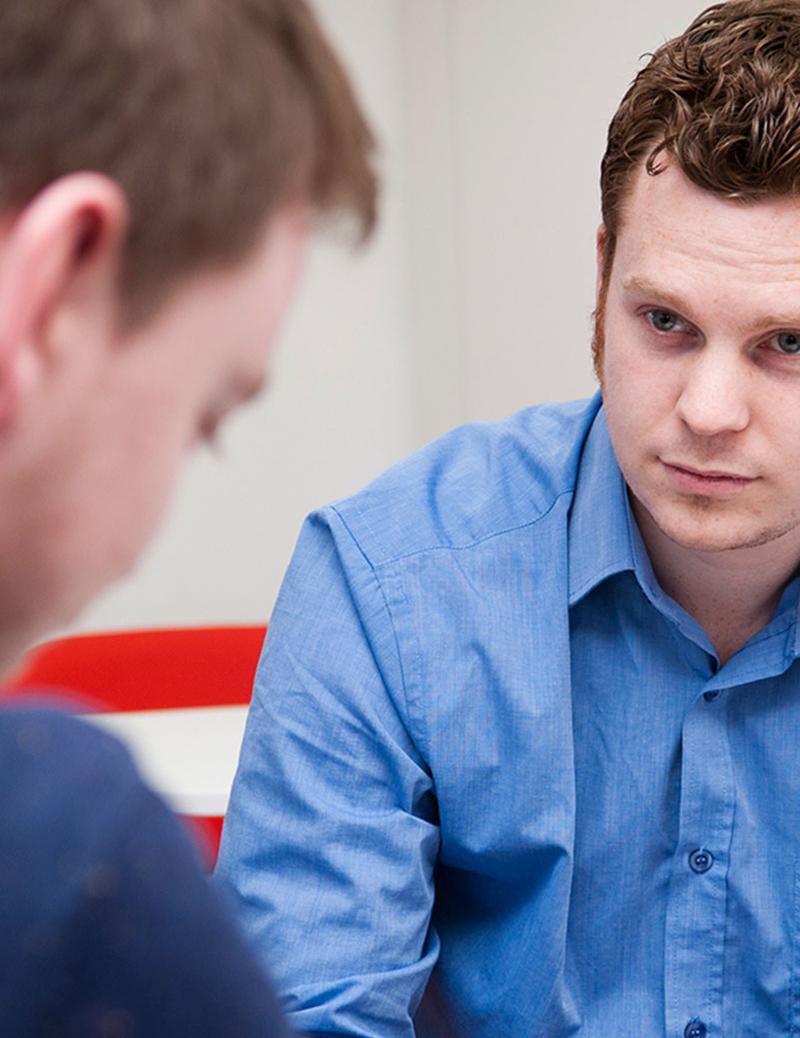 student sat in blue shirt sat down facing another man