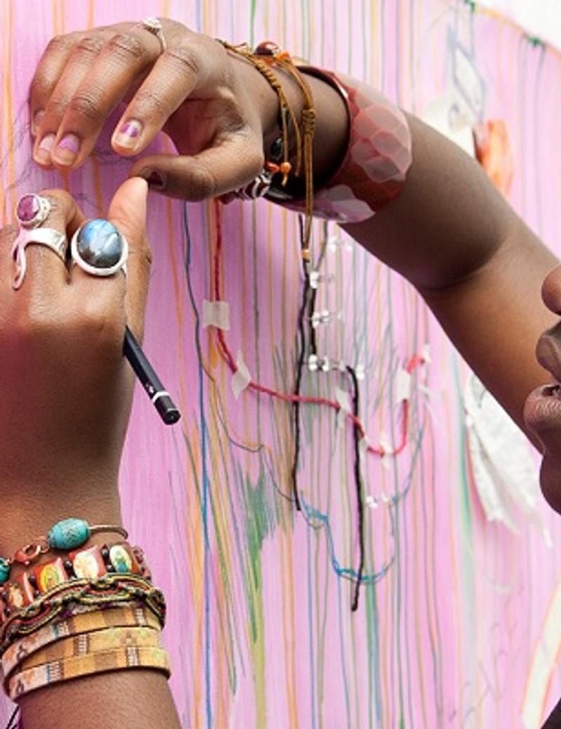 A woman artist adding vibrant colors to a pink wall with her paintbrush, creating an exquisite piece of art.