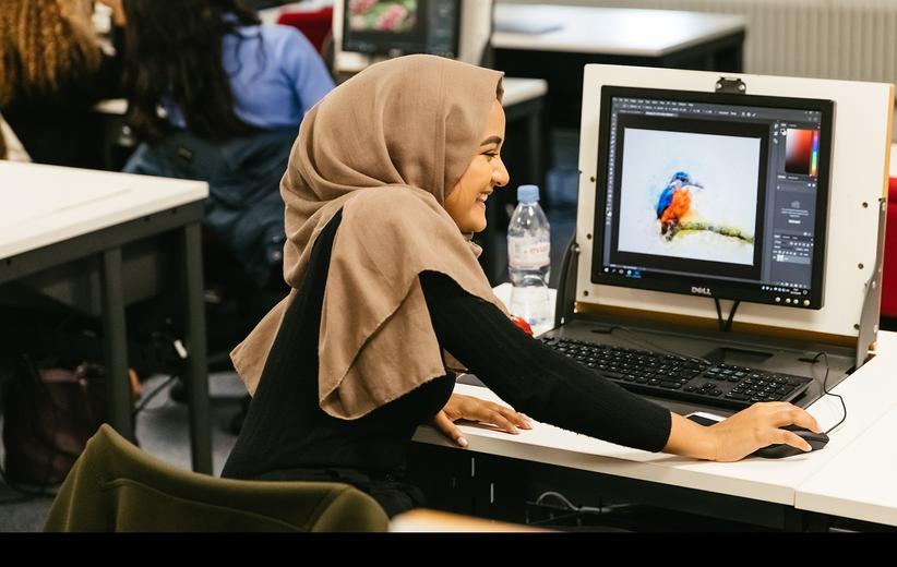 A woman wearing a hijab is focused on her computer screen as she works diligently.