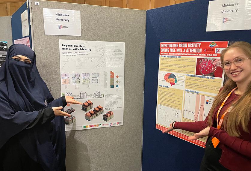Two students stand either side of a display of posters