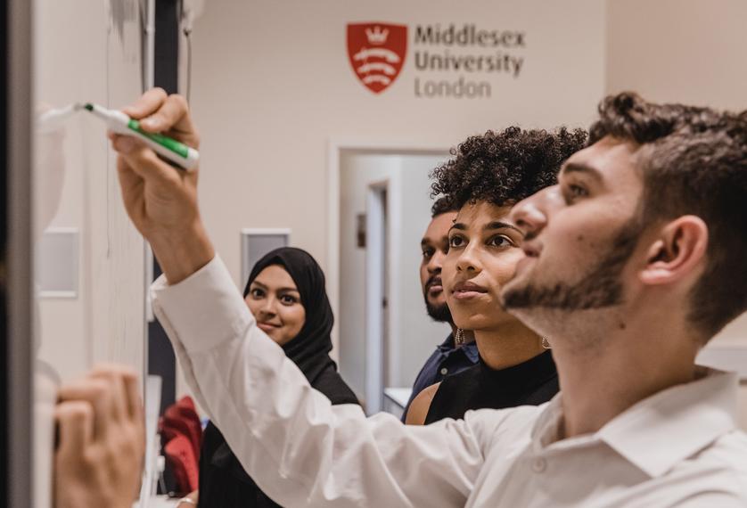 A group of students in discussion and writing on a whiteboard in a classroom