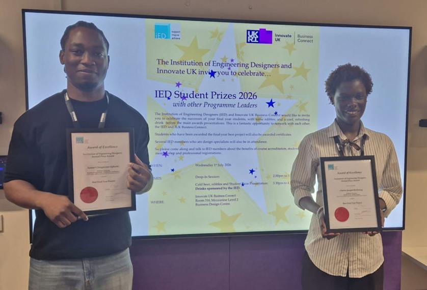 Two award winners holding certificates, with a screen behind them displaying their prize.